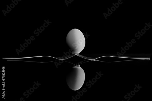 An egg balancing on two forks. Reflection on a black background.