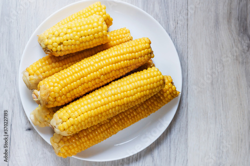 Boiled corn close up. Cobs of sweet juicy corn. Cobs of boiled corn on a plate. Sweet corn on the table. Grain background with free space. Vegetarian food. Cereal culture.