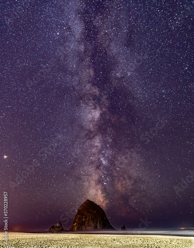 Vertical Image-Milky Way galaxy shines in the sky above Haystack Rock on Cannon beach in Oregon