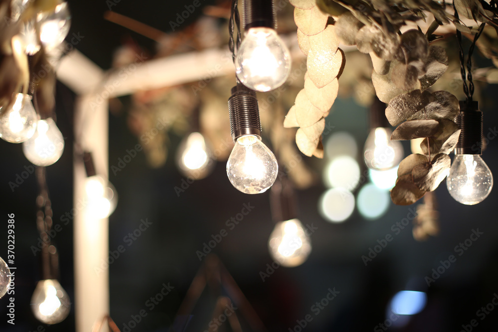 Light bulbs hanging on the ceiling among branches with dry leaves on a dark background Light bulbs hanging on the ceiling among branches with dry leaves on a dark background