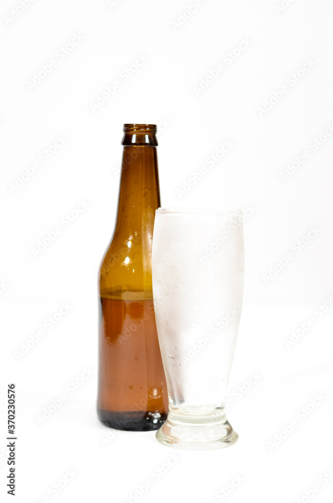 Brown glass bottle and a cold empty glass on a white background. Brown glass bottle and a cold empty glass on a white background.