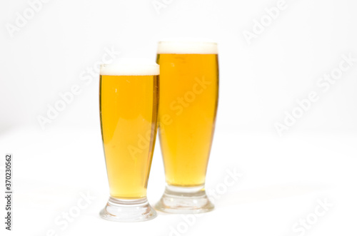 Two glasses full of beer with foam along on a white background.