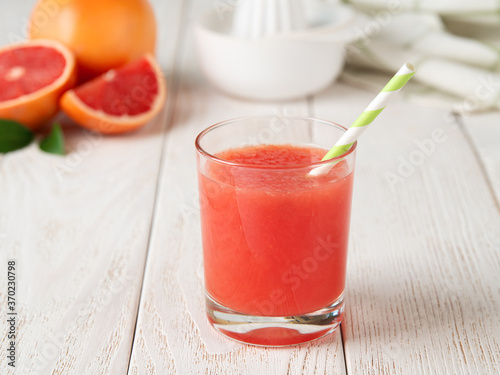 Glass of freshly squeezed grapefruit juice with pulp and drinking straw on a white wooden table. Vegetarian, raw food diet and healthy eating.