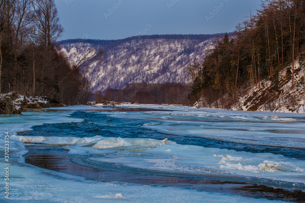 Fototapeta premium Northern landscape of Primorsky Territory, Samarga River. Frozen river in the taiga against the background of hills with coniferous trees at sunset