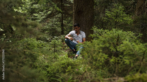 Handsome young man leaning on tree is dealing with wood stick in his hand , relaxation concept