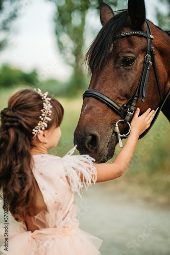 A little girl strokes a horse her favorite horse on the head. Communication of a child with a horse in the summer.