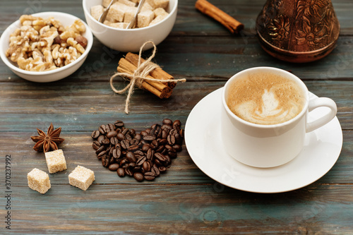 Nuts in the bowl, coffeepot, heart-shaped coffee beans, cinnamon, anise, sugar, and cap of coffee on wooden background