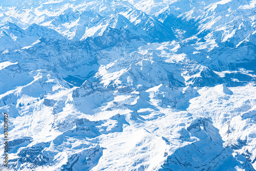 Blue planet earth unique alpine aerial panorama. High altitude aerial view of snow capped central European Alps, seen from an airplane cabin window. Enviromental conservation concept.