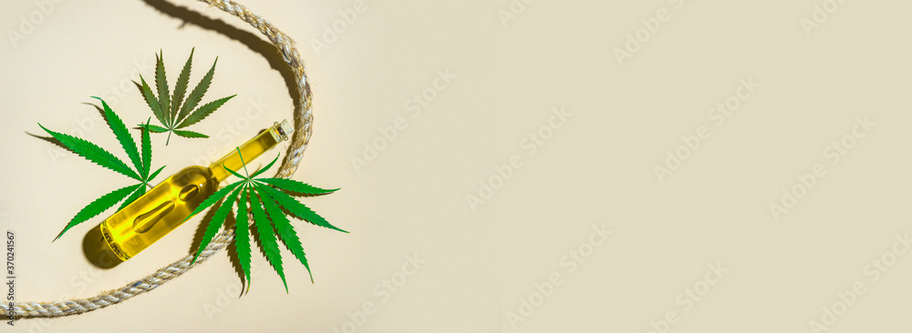 Naklejka premium Bottles with CBD oil, medical marijuana leaf and hemp rope on camel color background. Natural product concept.