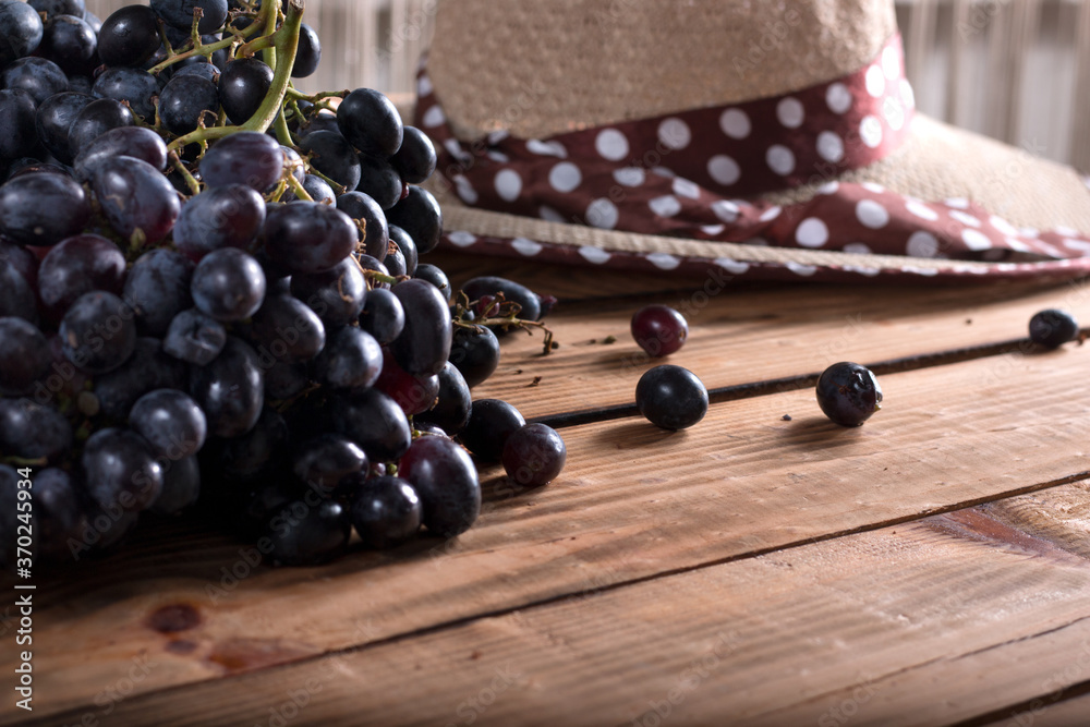 Bunches of fresh ripe red grapes on the surface with a wooden texture. Beautiful background with a branch of blue grapes in antique style. Red wine grapes. Bunches of fresh ripe red grapes on the surface with a wooden texture. Beautiful background with a branch of blue grapes in antique style. Red wine grapes.
