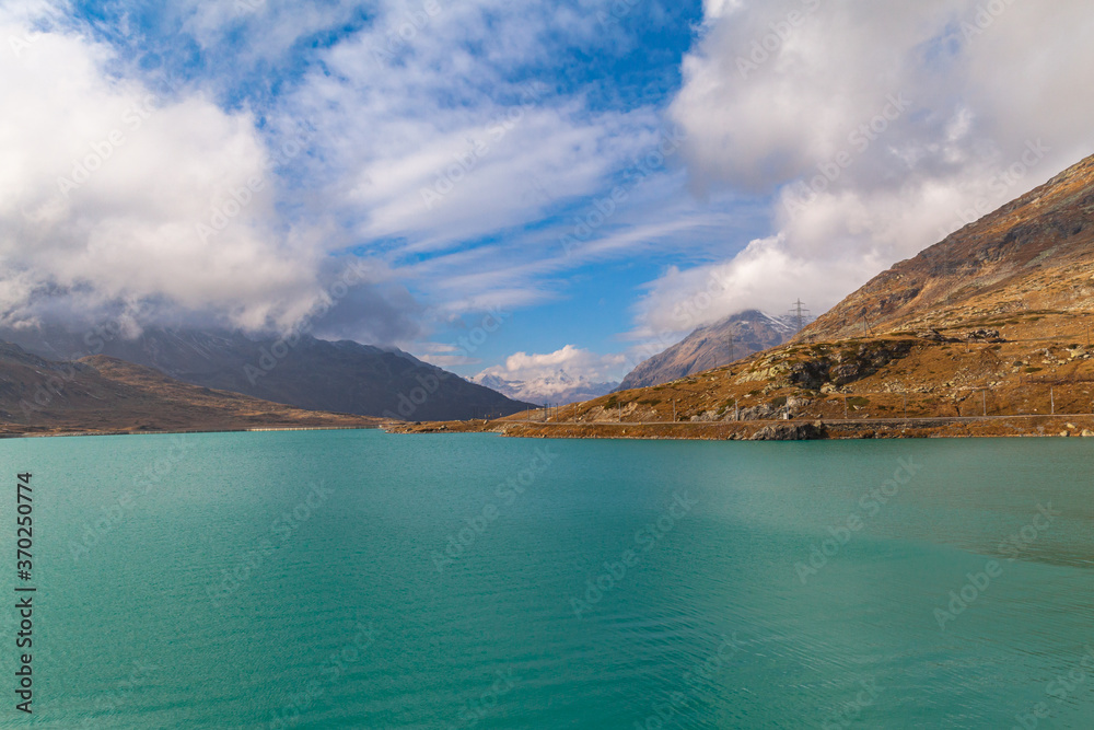 Panorama view of Lago Bianco lake and Swiss Alps on Bernina Pass the sightseeing train Bernina Express in autumn day with blue sky cloud, Canton of Grisons, Switzerland