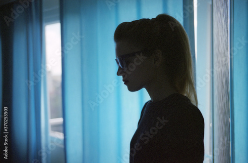 Close-up of a young caucasian CIA woman in black sun goggles standing in a room near blue curtains. Istanbul, Turkey.  Scanned film photo