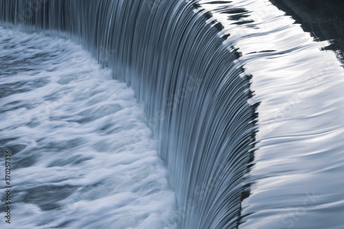 Falling water of a beautiful artificial waterfall in a garden in a public park. Summer.