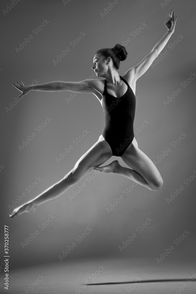 slim latin young woman, ballet dancer, jumping with arms and legs stretched out, with her hair tied back, studio black and white photo