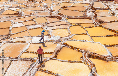 Two men at work collecting salt and salt bags in the famous salt terraces of Maras near the city of Cusco, Peru. photo