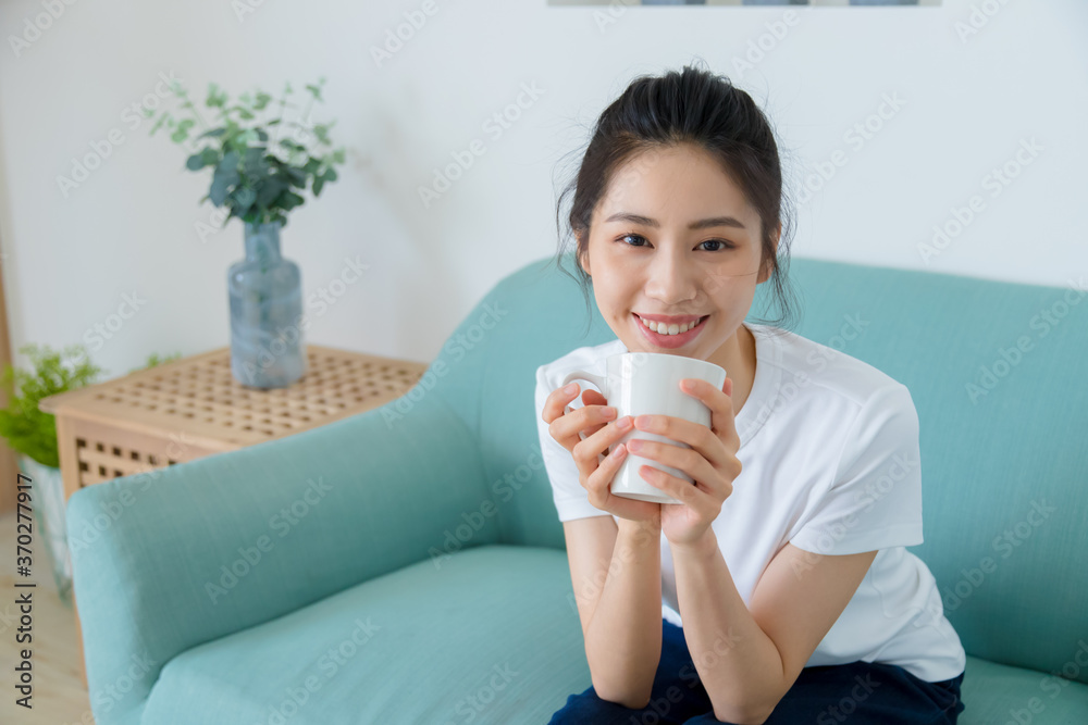 Young asia woman with ponytail in white t-shirt holding a cup of coffee or tea relaxing at home in the morning. Young asia woman with ponytail in white t-shirt holding a cup of coffee or tea relaxing at home in the morning.