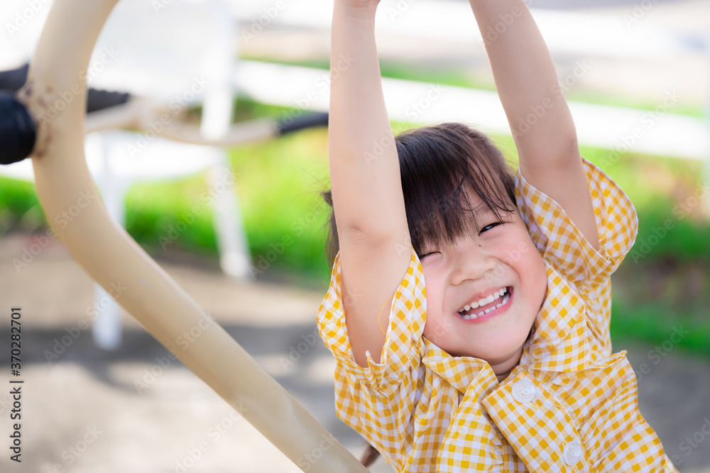 Obraz premium Happy kid hanging out with exercise machines on playground. Asian girl wearing yellow shirts are happy sweet smiling. Healthy child is 5 years old. Close up.