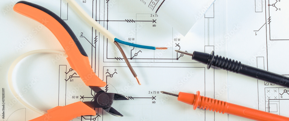 Cables of multimeter and pliers on construction drawings of house. Building home concept Cables of multimeter and pliers on construction drawings of house. Building home concept