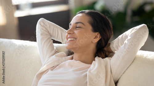 Head shot close up happy young attractive woman relaxing on comfortable couch with folded hands behind head, enjoying good mood stress free weekend leisure time indoors, visualizing future at home.