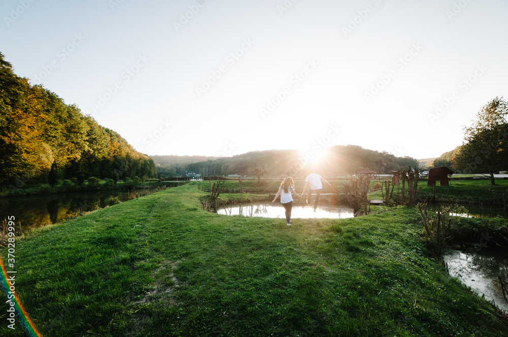 Couple holding hands walking away. Portrait of a romantic young man and woman in love in nature. husband and wife running through the field and holding hands over sunset.