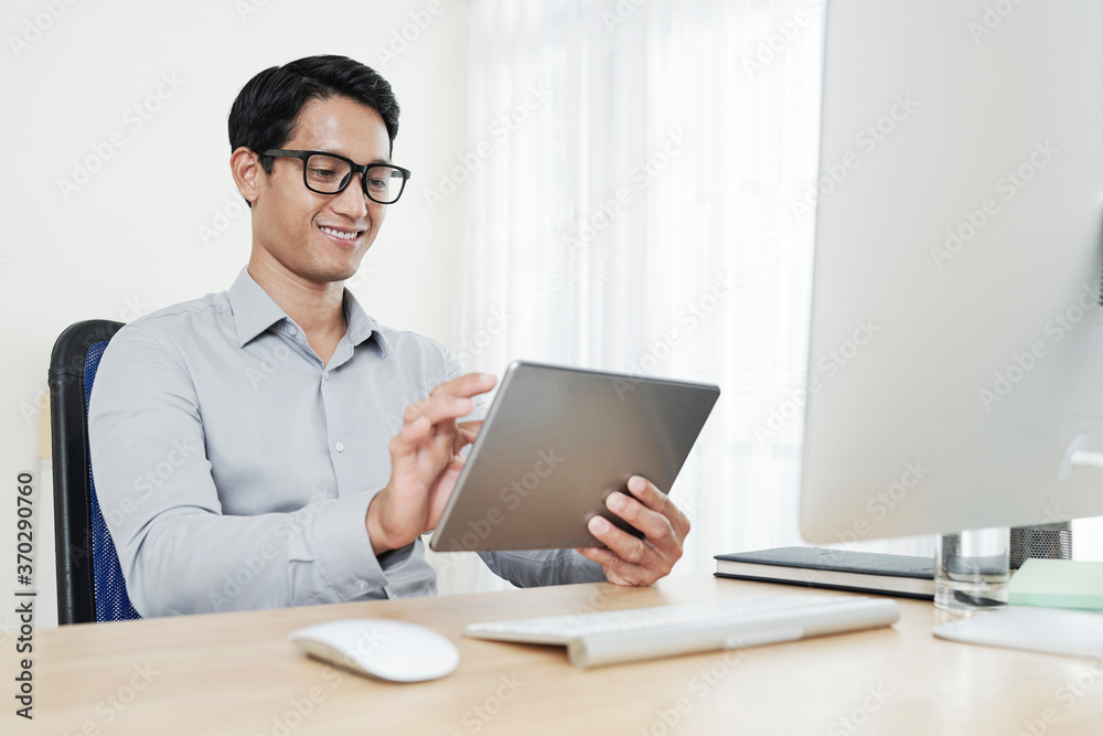 Handsome young Asian software developer testing application he created for tablet computer Handsome young Asian software developer testing application he created for tablet computer
