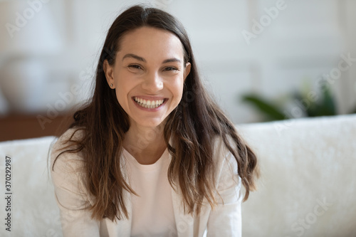 Portrait of happy young mixed race beautiful girl relaxing on cozy sofa. Smiling pretty millennial woman looking at camera  holding video call with friends  laughing at funny joke  profile picture.