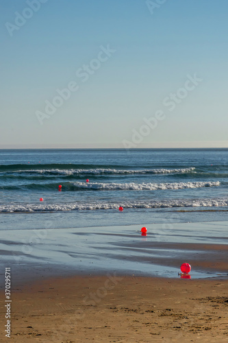 Red marker buoys on empty beach. Praia da Caparica, Portugal