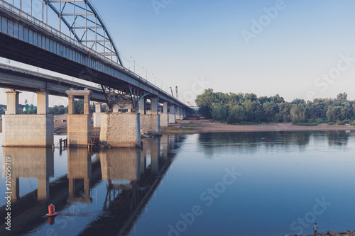 View of the bridge over the river. The structure is reflected in the water, on the other side of the river you can see the trees. There are no people. High quality photo