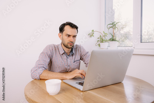 man in shirt with a cup of coffee works on laptop