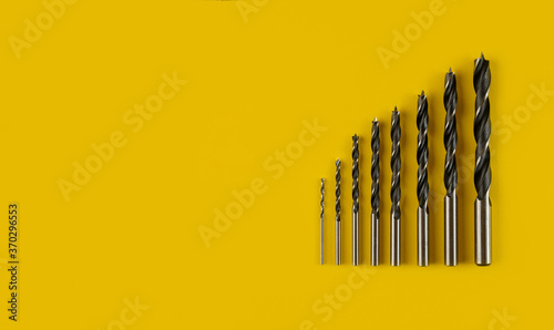 Drill bits of different sizes on yellow background,top view