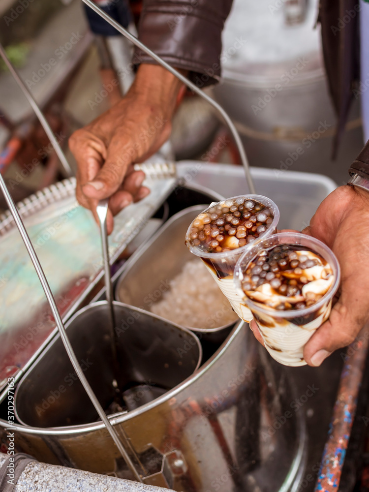 A vendor adding generous servigs of sugar syrup to 2 cups of Taho. Taho