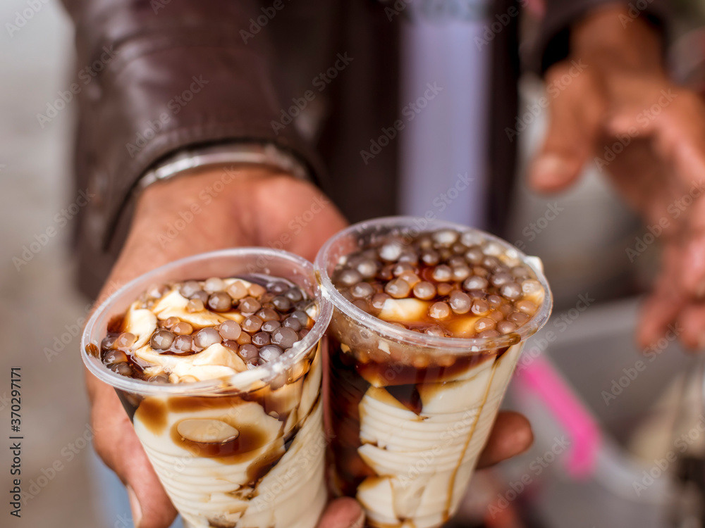 A man holding 2 cups of taho. Taho is a Philippine snack made of soft