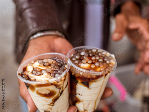 A man holding 2 cups of taho. Taho is a Philippine snack made of soft tofu, carmelized sugar and sago pearls. photo