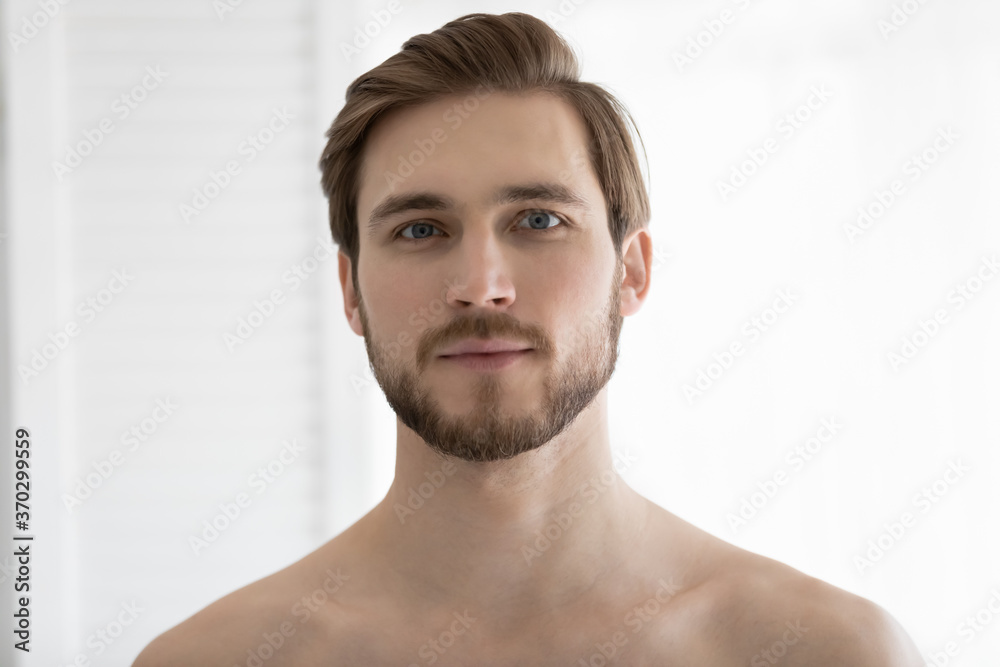 Obraz premium Head shot portrait handsome bearded young man with bare shoulders looking at camera, standing in bathroom at home after shower, personal hygiene, morning routine and skincare concept