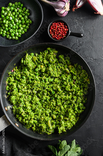 Mushy peas recipe cooked frying pan and peas in bowl with mint shallot pepper and salt on black stone surface  organic keto food top view close up