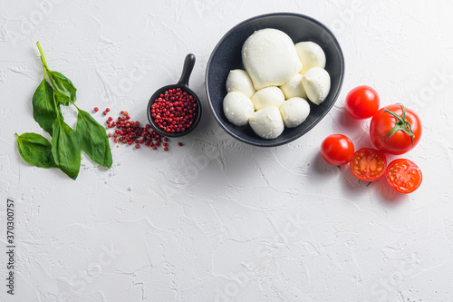 Raw ripe  Mozzarella cheese balls with fresh basil leaves and cherry tomatoes, the ingredients , on white background  top view space for text