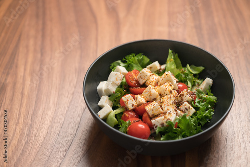 Healthy light salad with cherry tomatoes, mozzarella and frisee in black bowl on walnut surface