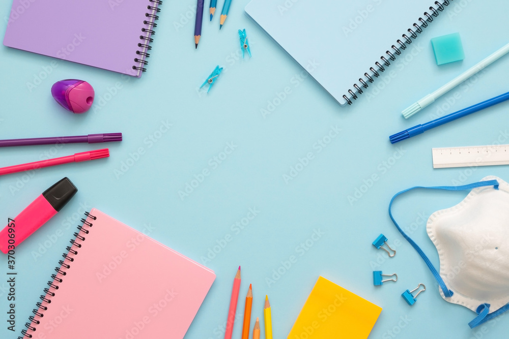 Colorful stationery set on the blue background. Top view of blue, pink and purple notebooks, paper clips, eraser, felt tip pens, color pencils, marker and face mask. Copy space. Back to school. Colorful stationery set on the blue background. Top view of blue, pink and purple notebooks, paper clips, eraser, felt tip pens, color pencils, marker and face mask. Copy space. Back to school.