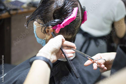Hairdressing services during coronavirus. Hairdresser in face mask cuts hair of woman in face mask. Hairdressers cutting hair during COVID-19