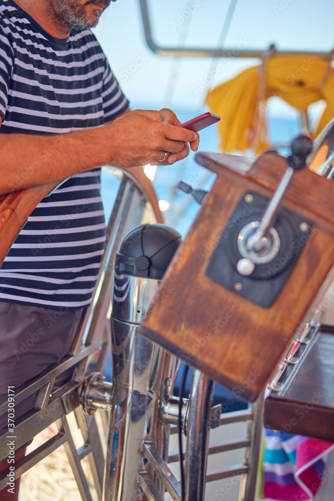 Sailing boat captain using smartphone for navigation on the open sea.