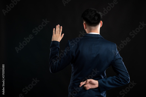 Back view of business man wearing blue business suit and tie taking oath showing fingers crossed