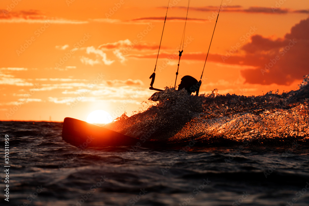 Silhouette of kitesurfer riding in beautiful orange sunset with the sun right behind
