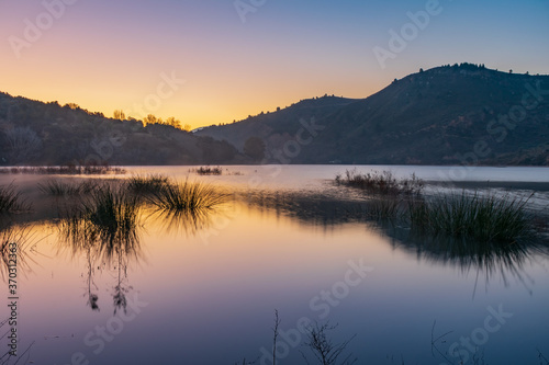 Landscape of a lake at sunrise with a clear sky reflected in the water.