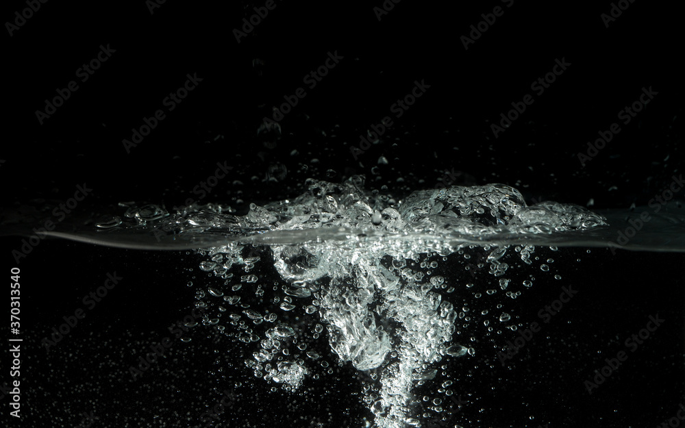 Water splashing as it's poured into aquarium tank, black background