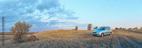 A blue car stands on a hill next to a country road  the concept of car travel. Panorama  selective focus.