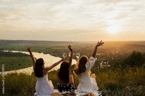 Obraz na płótnie Three best girlfriends having fun together on a picnic on the mountain at sunset. They enjoying time in nature at weekend. Copy space. w salonie