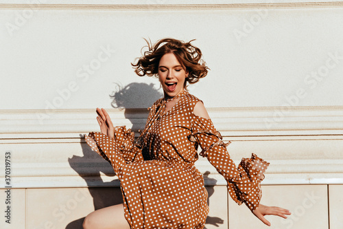Jocund brown-haired woman dancing on the street. Portrait of emotional european girl in brown dress.