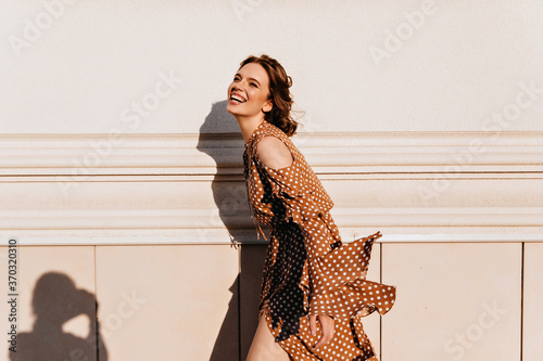 Excited spectacular woman posing in warm september day. Outdoor shot of laughing brown-haired girl in vintage dress.