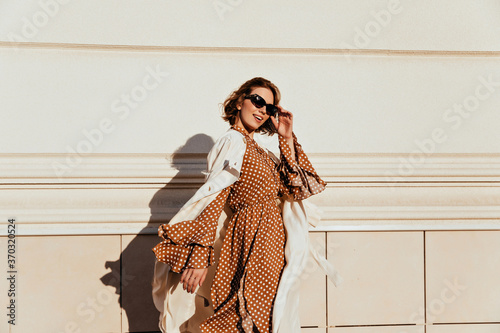 Pretty woman in long brown dress enjoying sunny day. Lovable white girl in retro attire walking down the street.