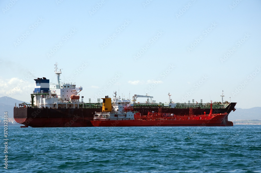 A chemical tanker which is anchored being refuelled by a fuel barge at sea